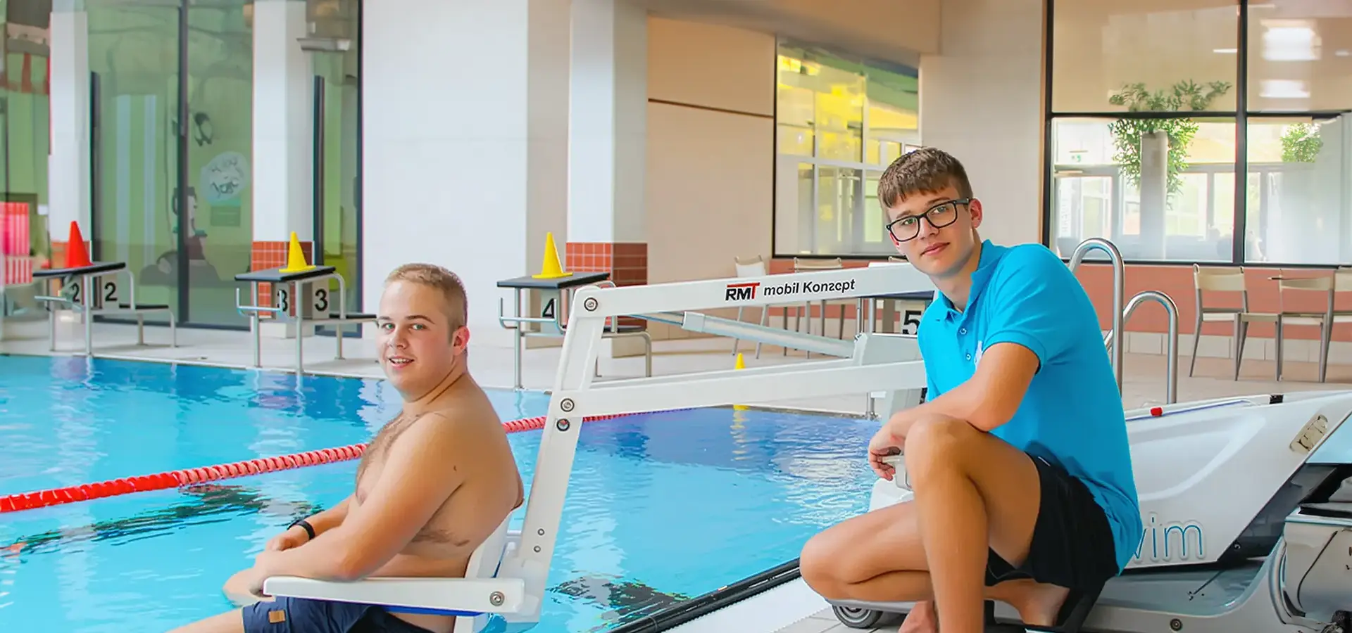 Ein Mitarbeiter hilft einem Mann im Rollstuhl mit einem Schwimmbadlifter ins Wasser