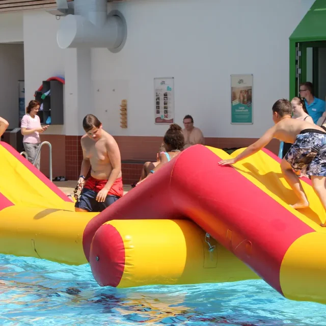 Mehrere Personen spielen auf bunten Luftmatratzen in einem Hallenbad.