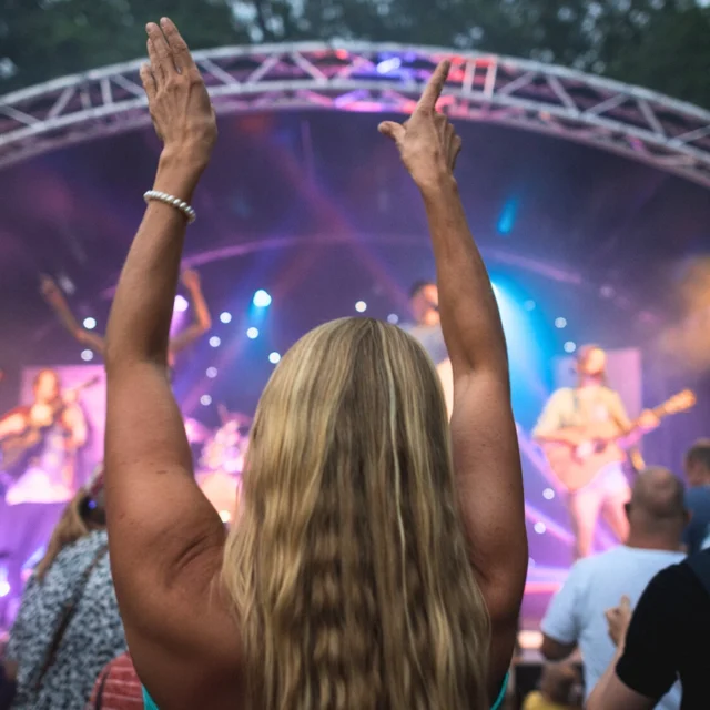 Blonde Frau tanzt vor einer Bühne zu einem Konzert