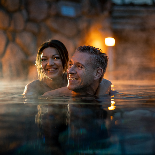 Paar schwimmt in der Dämmerung im Schwimmbecken des Saunagartens